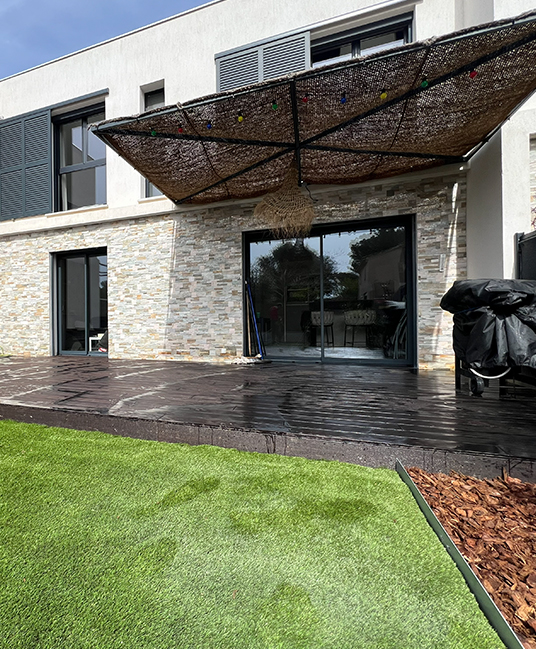 Terrasse en bois sous voile d’ombrage, gazon et bordure de galets