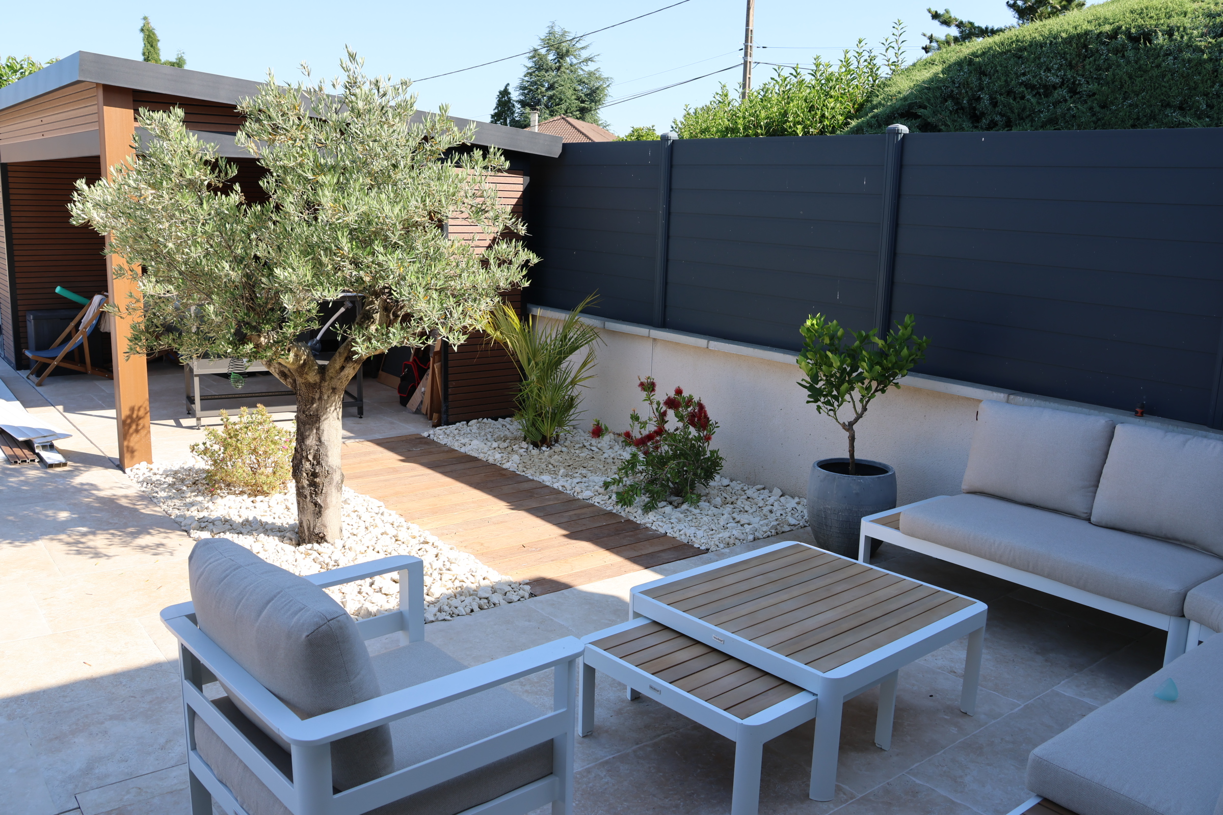 Terrasse aménagée avec salon de jardin, olivier et clôture occultante