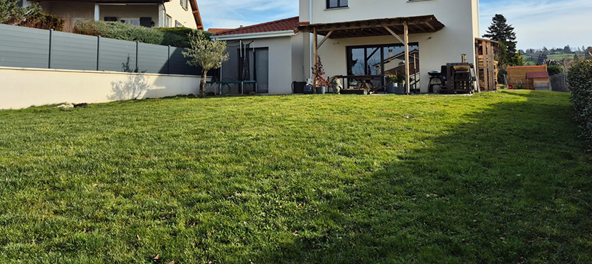 Grande pelouse tondue devant une maison avec terrasse couverte